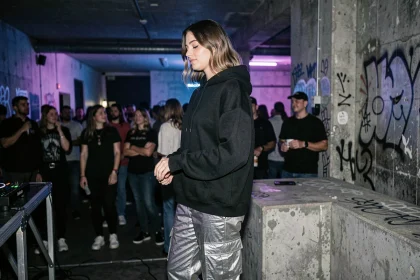 Jeune femme en tenue techno dans un club underground avec ambiance béton et lumières ultraviolettes